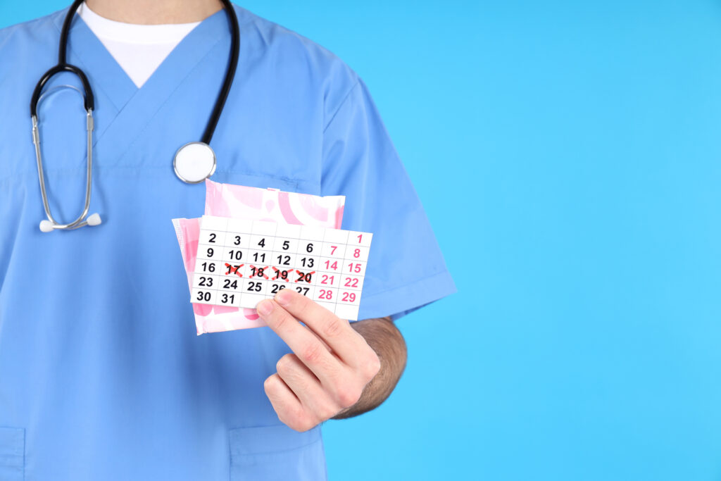 Doctor holds menstrual calendar and pads on blue background